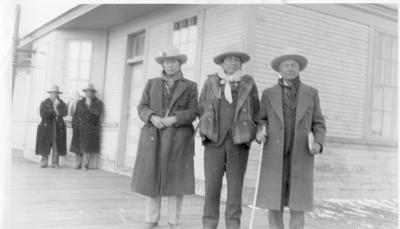 Black and white photo of three men posing for a photo on the train depot platform.