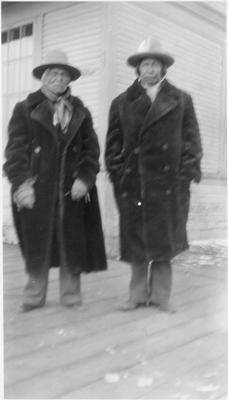 Black and white photo of two men posing for a photo outside of the train depot.