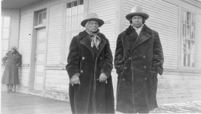 Black and white photo of Night Shoot and Charlie Iron Breast posing for a photo and Cecile Big Beaver in the background.