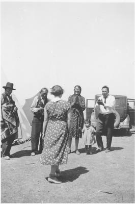 Black and white photo of a crowd with one person performing including Middle Rider, Bird Rattle, Cecile Boy and Oscar Boy, Browning, Montana, 1935