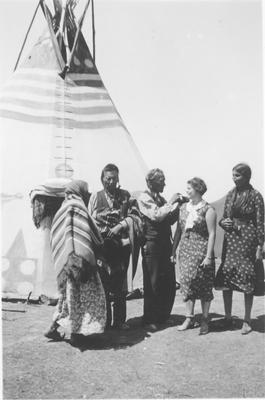 Black and white photo of a group of people standing in front of a tipi, Browning, Montana