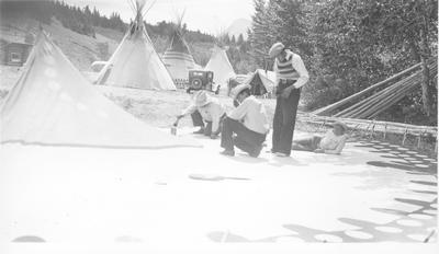 Black and white photo of 4 men painting and assembling tipis, Saint Mary
