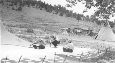 Black and white photo of 3 men constructing a tipi, Saint Mary