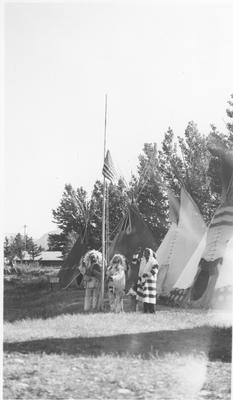 Black and white photo of a group of men in ceremonial dress raising the American flag, Saint Mary