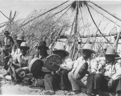 Black and white photo of a group of men sitting and playing drums, part of the Sun Lodge Ceremonies, Browning, Montana, 1927