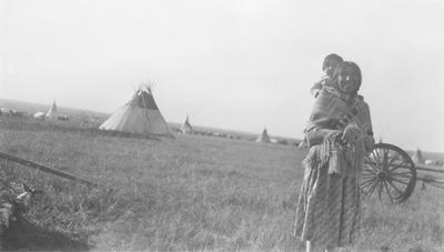Black and white photo of Mrs. Little Dog with a child on her back, Alberta, Canada