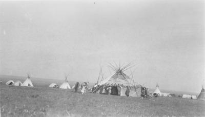 Black and white photo of a lodge in the middle of a tipi encampment, Belly Buttes, Alberta, 1927