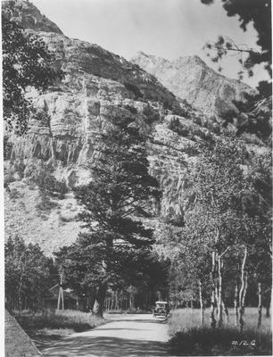 Black and white photo of an automobile driving on a road in Glacier National Park, 1920s