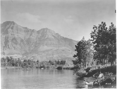Black and white photo of a woman sitting on the edge of a lake in Glacier National Park.