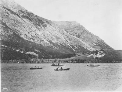 Black and white photo of 4 boats out on a lake in Glacier National Park.