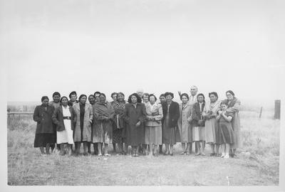 Photo of a large group of men and women standing in an open field.