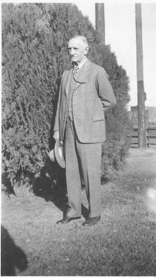 Photo of James Willard Schultz as an Old Man Standing in Front of a Large Hedge