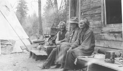 Two Men and a Woman Sitting on a Camp Bench by a Log House