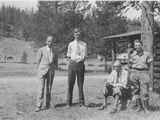 Photo of Two Older Men and Two Young Men Standing in Front of a Log Cabin