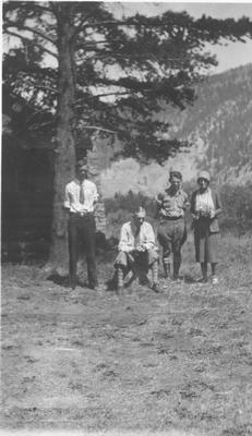 A Man Sits on a Rock with Two Young Men and a Woman, Near the Front of a Log Cabin