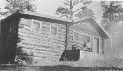 Man and Cat Sit on the Porch of a Hunting Lodge