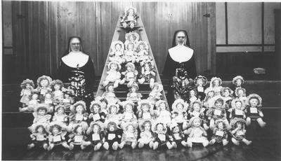 Two Nuns Stand Behind a Table Full of Dolls