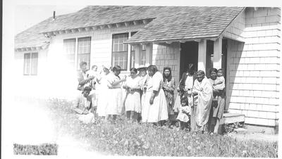 Group of Women and Children Stand in Front of a White Clapboard Building