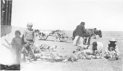 Two Young Boys Play While Two Women Bag Wool for Market