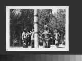 Photo of Men in Ceremonial Dress Dancing Around the Center Pole of a Lodge.