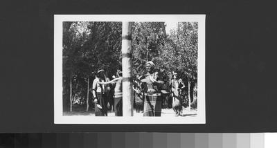 Photo of Men in Ceremonial Dress Dancing Around the Center Pole of a Lodge.