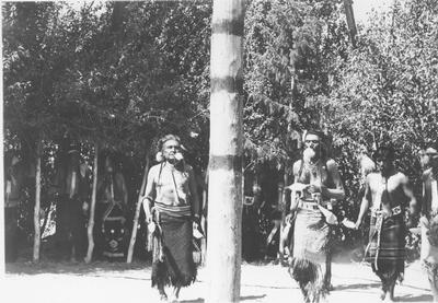 Photo of four men including, John LeClair, James Wetchi and Louis Enos, wearing ceremonial dress and dancing near the center post during a ceremony