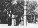 Photo of a man in ceremonial dress standing behind three women in front of the center post during a ceremony