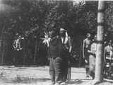 Photo of a large group of men in ceremonial dress standing behind a man in plain clothes