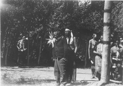 Photo of a large group of men in ceremonial dress standing behind a man in plain clothes