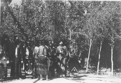 Photo of a group of men in ceremonial dress waving feathers they carry in their mouths