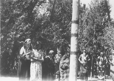 Photo of a group of people surrounding the center post of a ceremonial lodge